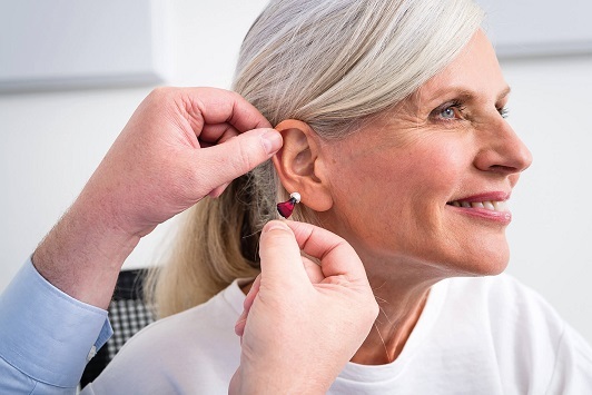 Seniorin bekommt ein modernes Hörgerät ins Ohr eingesetzt, Hörakustiker Beratung.